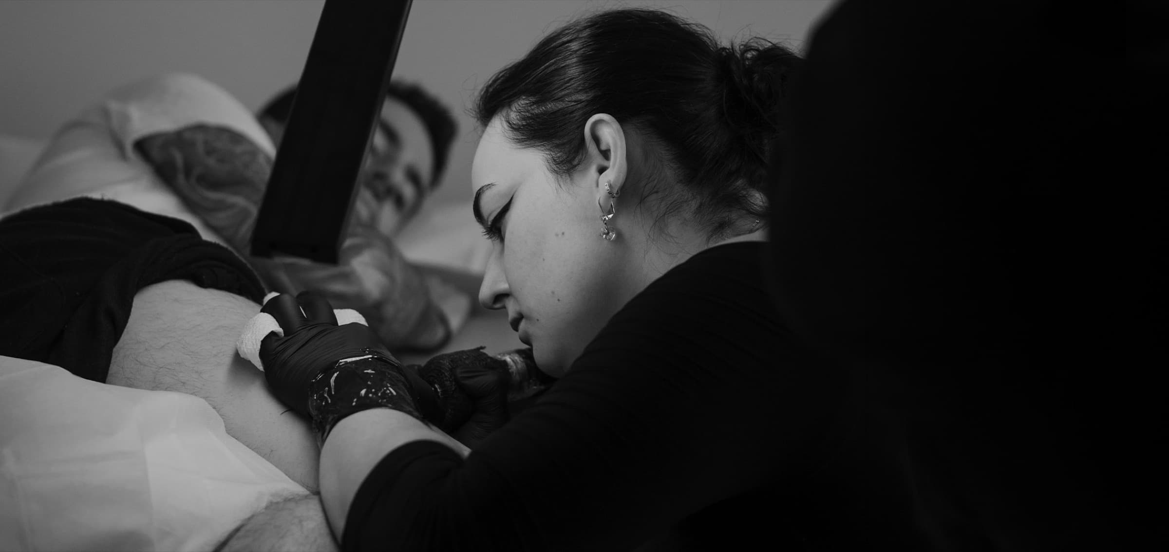 Emma Vanboxtel leaning in close while tattooing a client