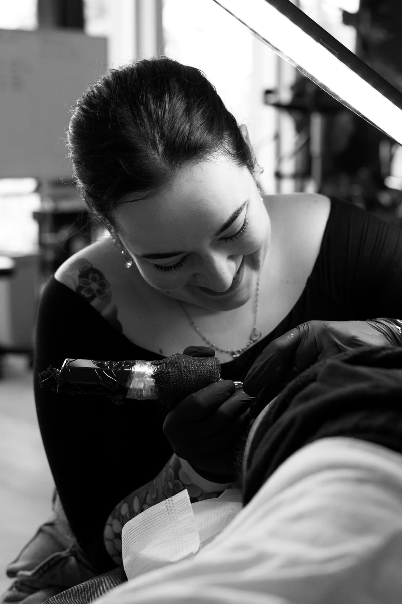 Emma Vanboxtel leaning in over a client's arm, mid-session at the studio